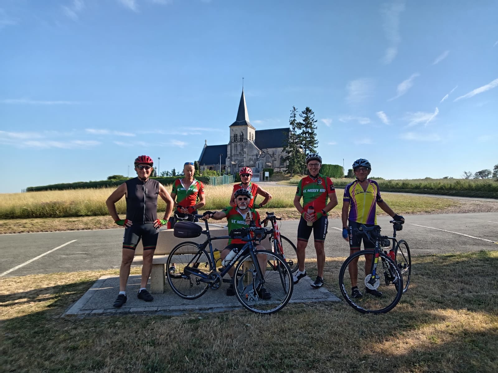 Six cyclistes du Vélo Club de Mouy posant avec leurs vélos pendant la pause fraîcheur devant l'église de Saint-Sulpice, dans la campagne de l'Oise