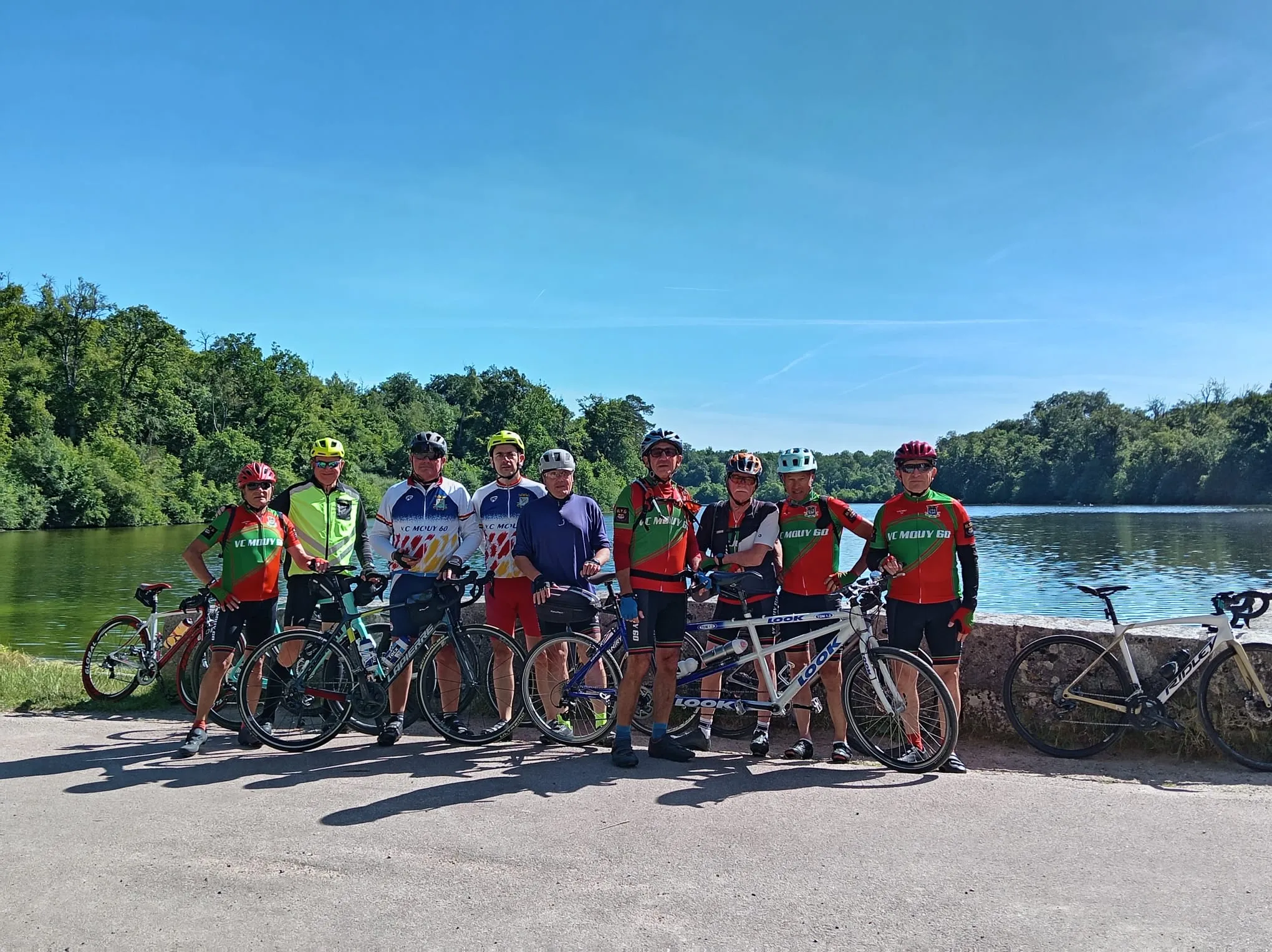 Les neuf cyclistes du VC Mouy, dont un tandem, posant avec leurs vélos devant un plan d'eau lors de la rando de la Nonette