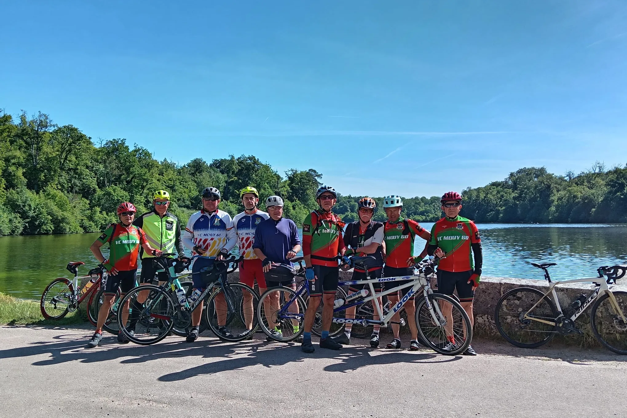 Les neuf cyclistes du VC Mouy, dont un tandem, posant avec leurs vélos devant un plan d'eau lors de la rando de la Nonette le 14 juin 2026