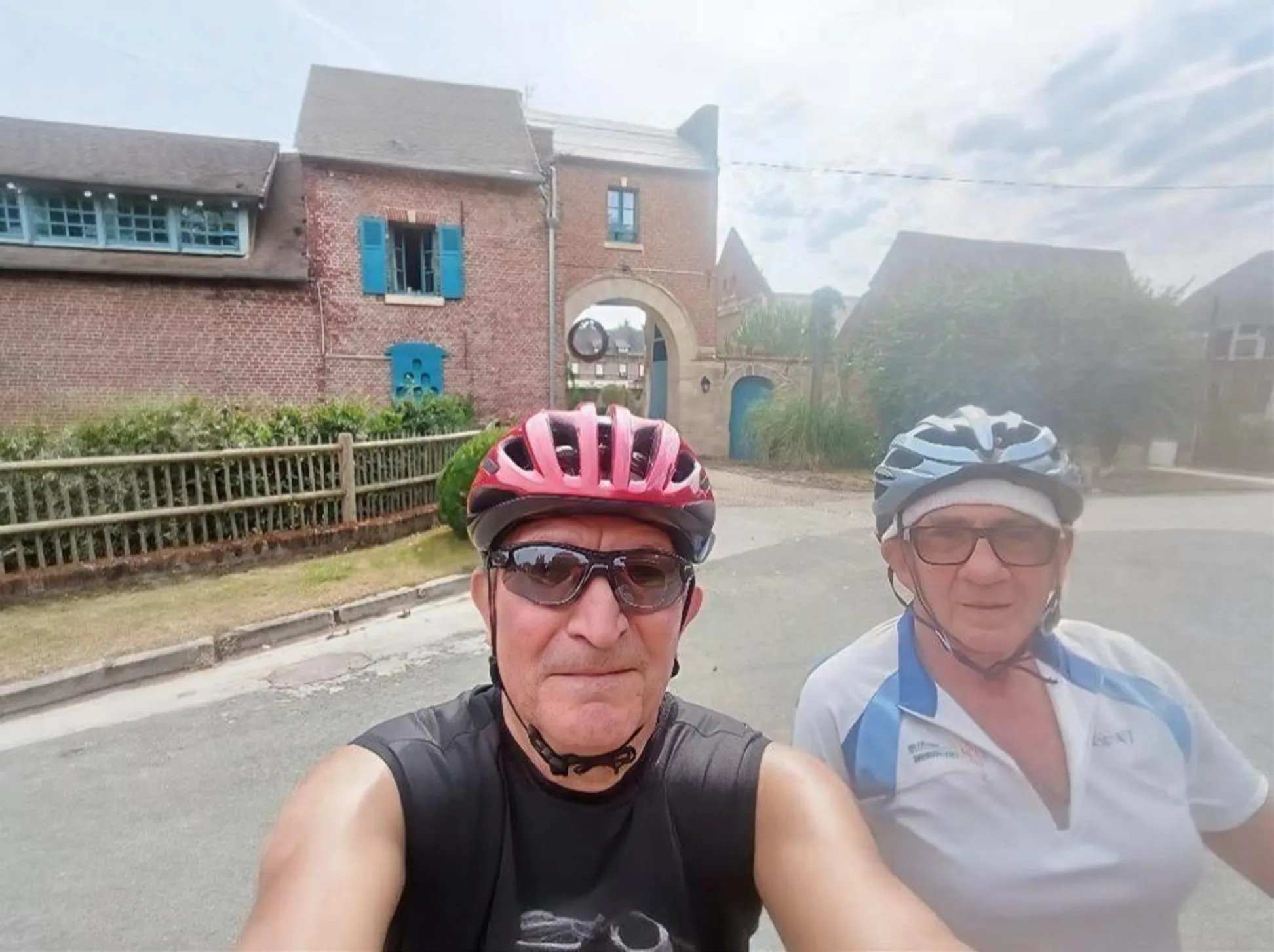 Selfie de deux cyclistes du Vélo Club de Mouy casqués devant une ferme picarde à porche, lors de leur sortie vers Saint-André-Farivillers